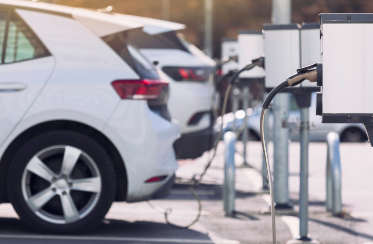 An image of several electric vehicles (EVs) charging at a modern charging station. The scene is set in a clean, urban environment, with sleek, eco-friendly cars plugged into high-tech chargers. The station is well-lit, showcasing the advanced infrastructure supporting sustainable transportation.